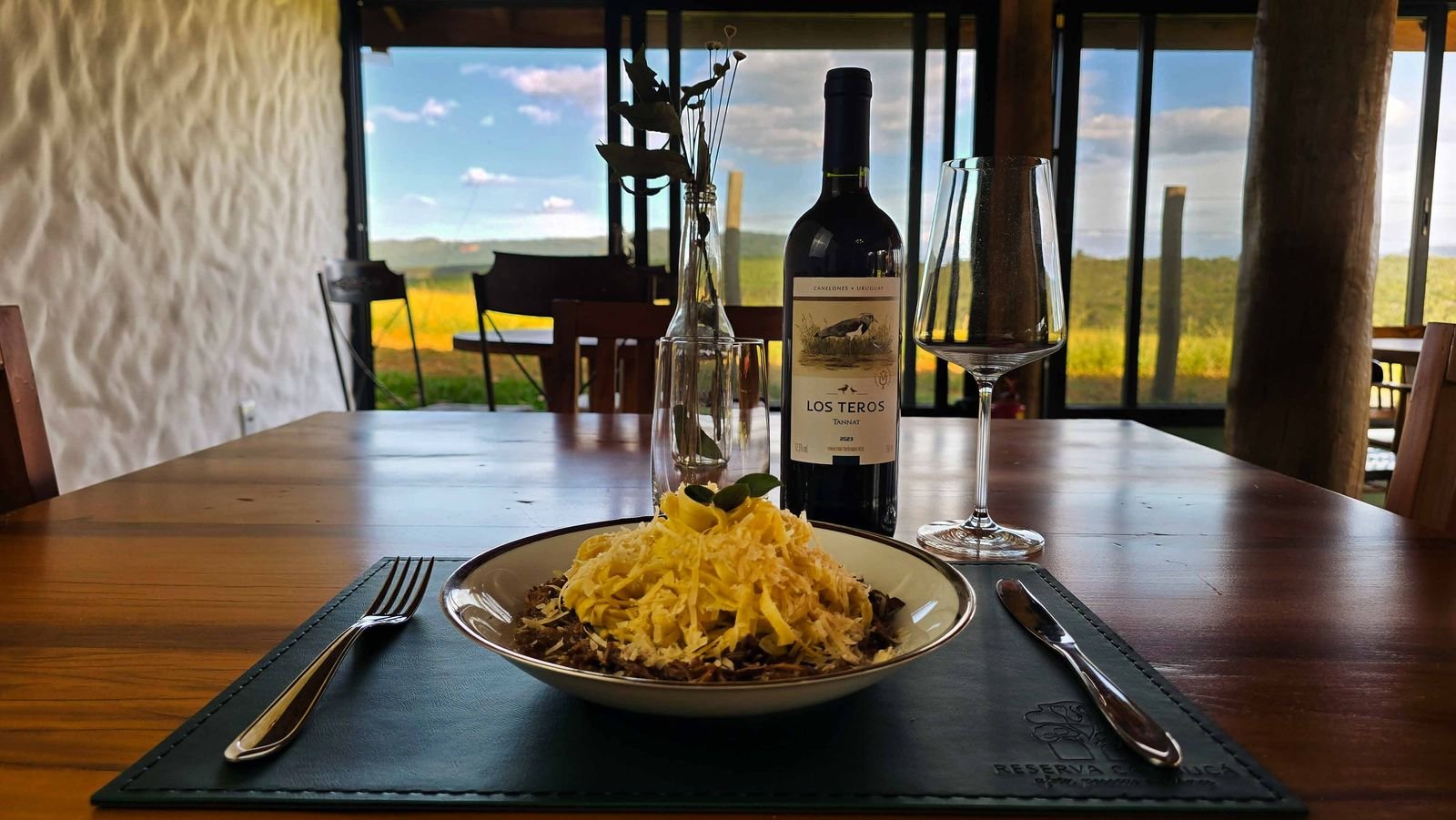Prato servido à mesa de madeira no restaurante da Pousada Reserva Cambucá, com taça e vista para a serra